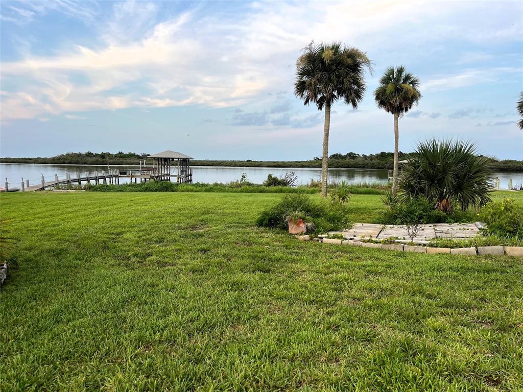 A grassy backyard features two palm trees, a wooden dock, and a gazebo overlooking water — 281 GOLDEN BAY BOULEVARD, OAK HILL, FL