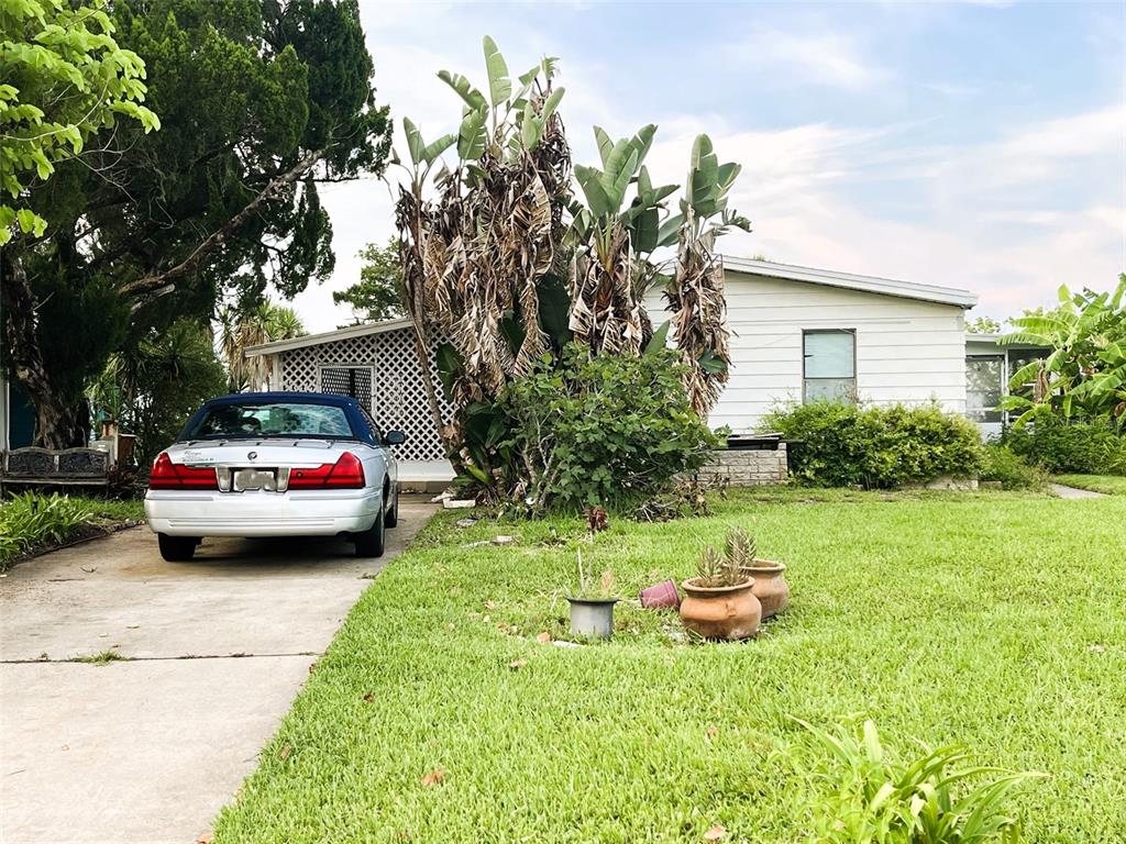 A silver sedan is parked in the driveway of a white house with large plants — 281 GOLDEN BAY BOULEVARD, OAK HILL, FL