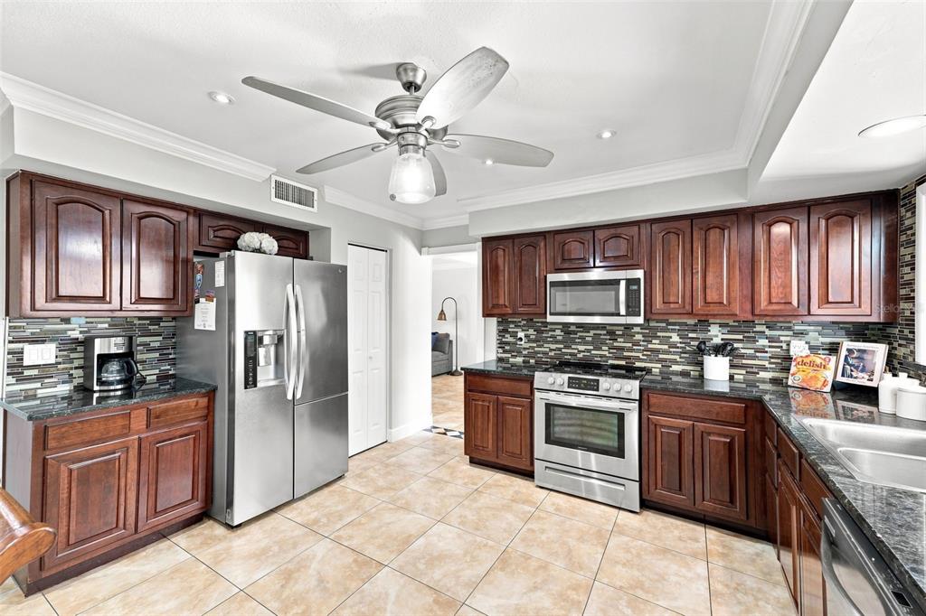 A kitchen features dark wood cabinets, stainless steel appliances, tile flooring, and a ceiling fan — 7314 WOODKIRK COURT, TAMPA, FL