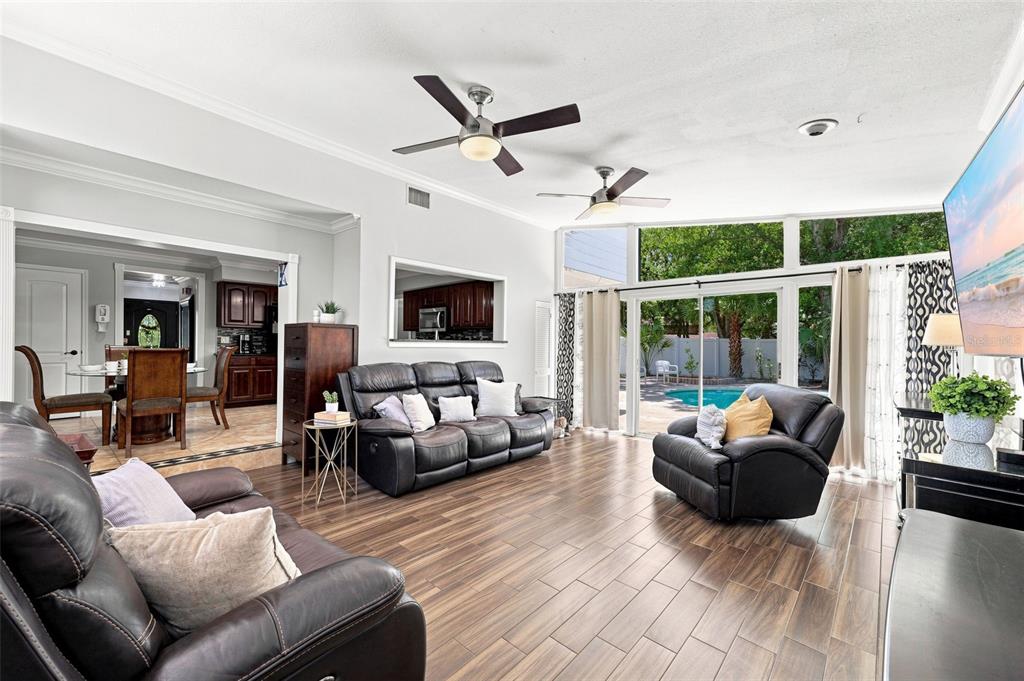 A living room with dark leather furniture, wood-look tile floors, and a view of a pool — 7314 WOODKIRK COURT, TAMPA, FL