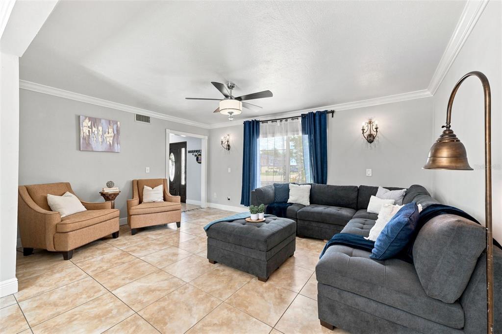A living room features tile flooring, a gray sectional sofa, two tan armchairs, and curtains — 7314 WOODKIRK COURT, TAMPA, FL
