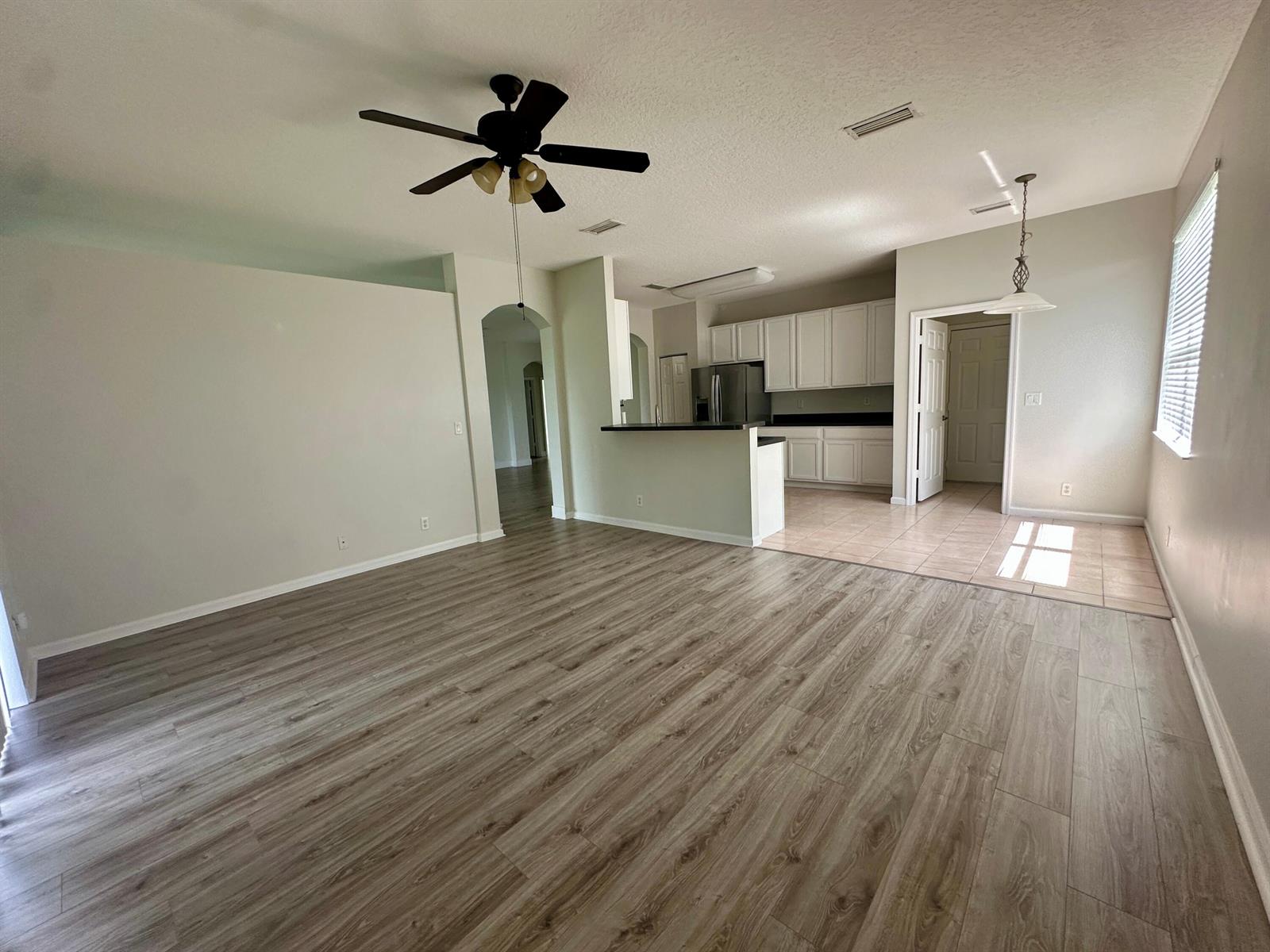 An open-concept living area features wood-look flooring, a ceiling fan, and an adjacent kitchen — 6075 46th Lane, Vero Beach FL 32967, VERO BEACH, FL
