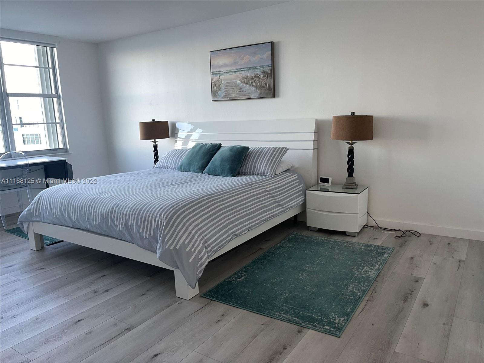 A bedroom features a white bed frame, striped bedding, two nightstands, and light wood flooring — 5161 Collins Ave # 914, Miami Beach FL 33140, MIAMI BEACH, FL