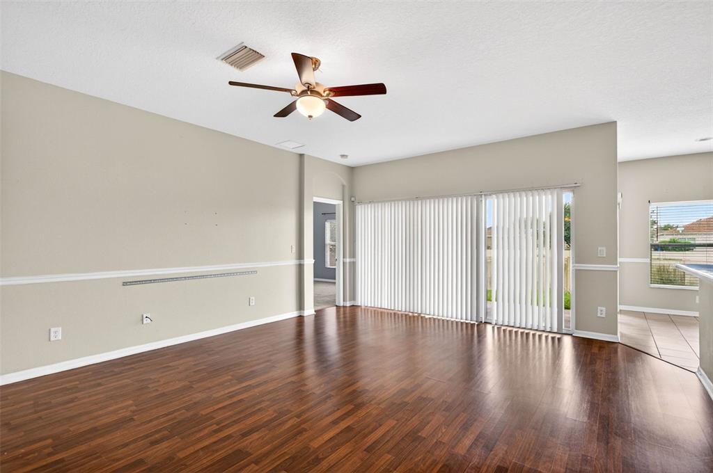 An empty living room features dark wood flooring, beige walls, a ceiling fan, and vertical blinds — 612 MARION HILL LANE, RUSKIN, FL