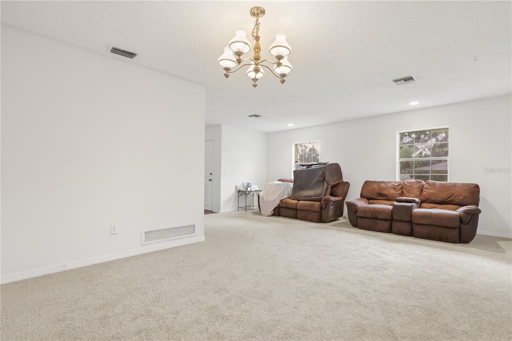 A living room with beige carpeting, white walls, a chandelier, and two brown leather sofas — 5310 NADINE STREET, ORLANDO, FL