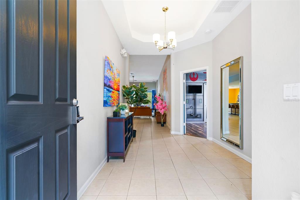 A tiled entryway leads into a home with a chandelier, a mirror, and wall art — 7743 COMROW STREET, KISSIMMEE, FL