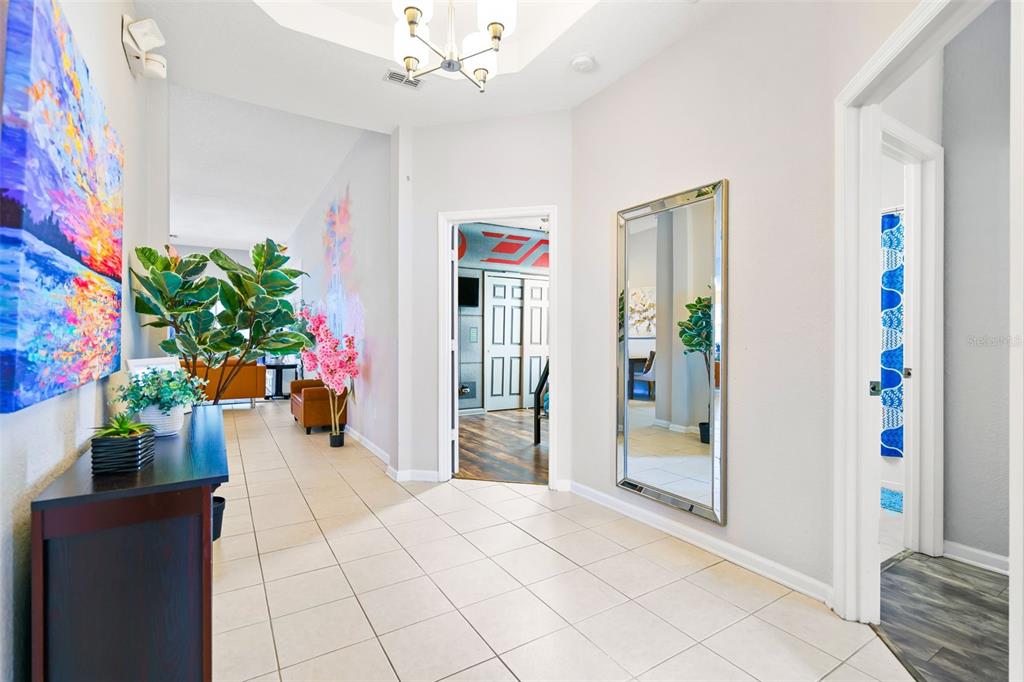A bright entryway features tiled floors, a large wall mirror, and a dark console table — 7743 COMROW STREET, KISSIMMEE, FL