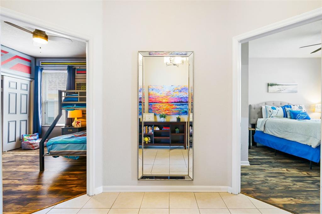A hallway with a full-length mirror between two bedrooms featuring wood-look flooring and tile — 7743 COMROW STREET, KISSIMMEE, FL