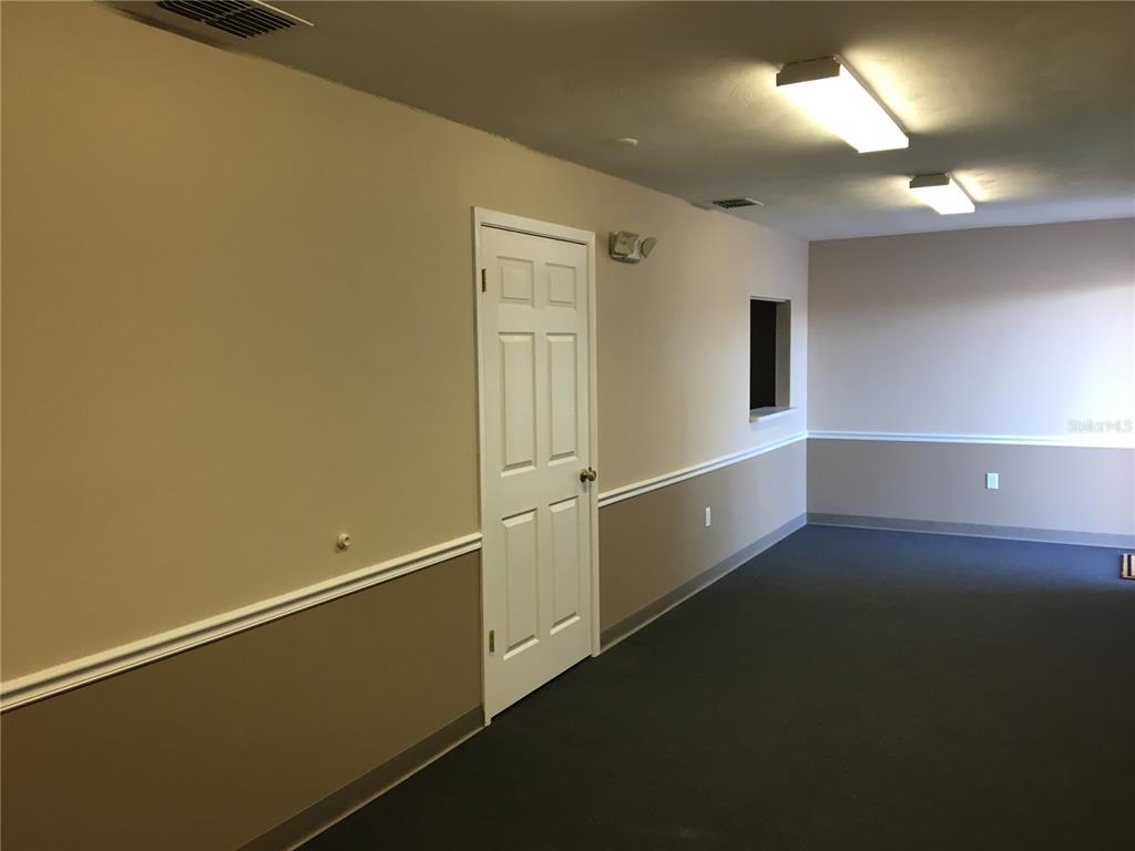 An interior view of a room with beige walls, a white door, and dark carpeting — 13910 FIVAY ROAD UNIT 10, HUDSON, FL