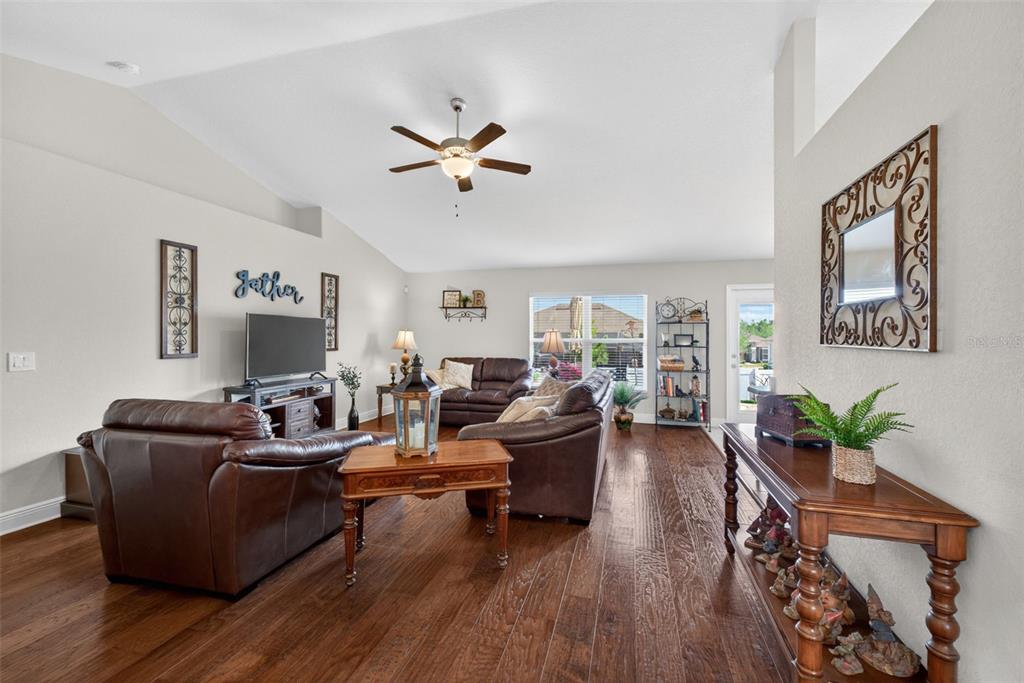 A living room features dark leather furniture, hardwood floors, and a vaulted ceiling with a fan — 2429 TWIN LAKE VIEW ROAD, WINTER HAVEN, FL
