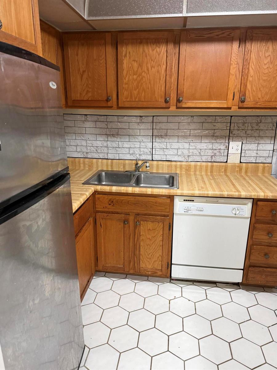 A kitchen features wood cabinets, a laminate countertop, a stainless steel sink, and hexagonal floor tiles — 3730 Inverrary Drive # 2a, Lauderhill FL 33319, LAUDERHILL, FL