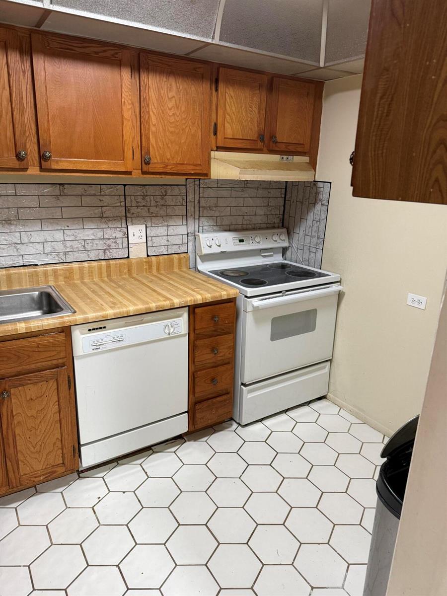 A kitchen features wood cabinets, a white dishwasher, a white stove, and hexagonal floor tiles — 3730 Inverrary Drive # 2a, Lauderhill FL 33319, LAUDERHILL, FL