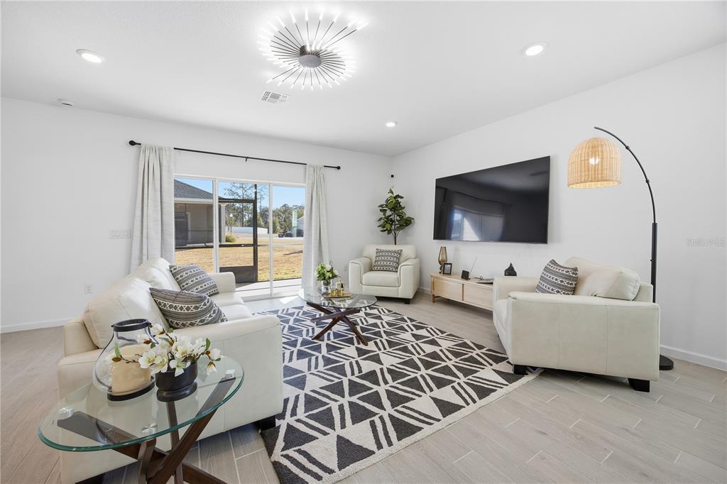 A bright living room features white furniture, a geometric rug, and a large wall-mounted television — 7561 SW 76TH TERRACE, OCALA, FL