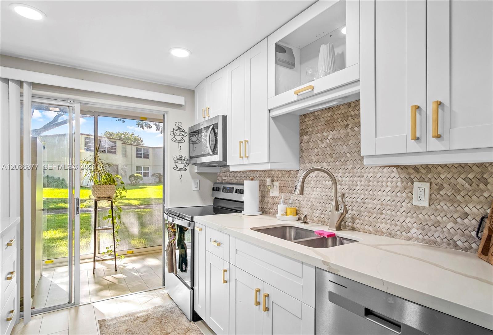 A modern kitchen features white cabinets, gold hardware, a herringbone backsplash, and a sliding door — 19 Abbey Ln # 104, Delray Beach FL 33446, DELRAY BEACH, FL