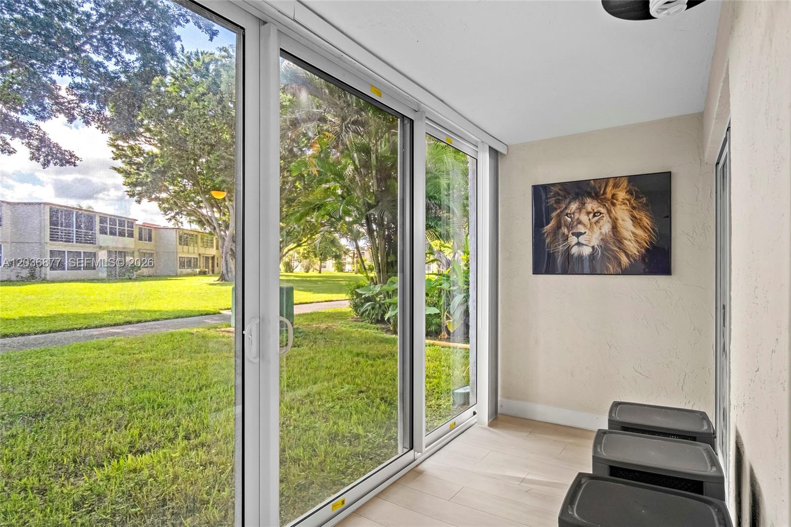 A sunroom features sliding glass doors, light wood-look flooring, and a lion wall art piece — 19 Abbey Ln # 104, Delray Beach FL 33446, DELRAY BEACH, FL