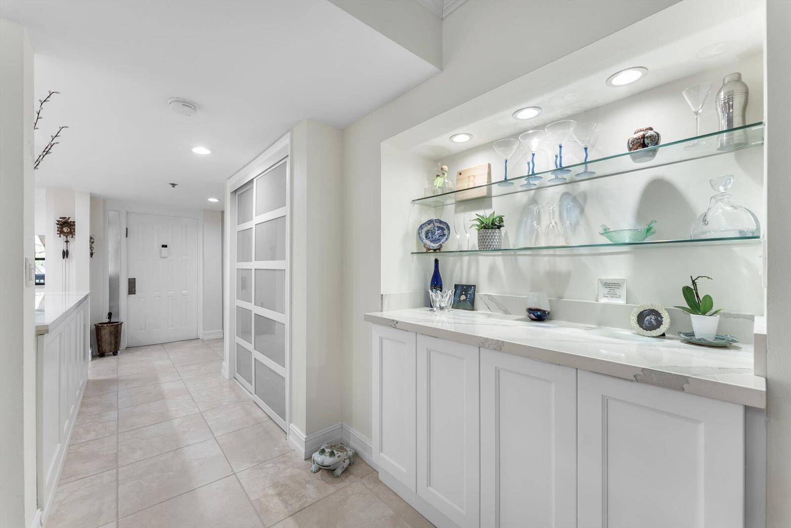 A hallway features a white built-in wet bar with glass shelves and marble countertops — 6420 Boca Del Mar Drive # 201, Boca Raton FL 33433, BOCA RATON, FL