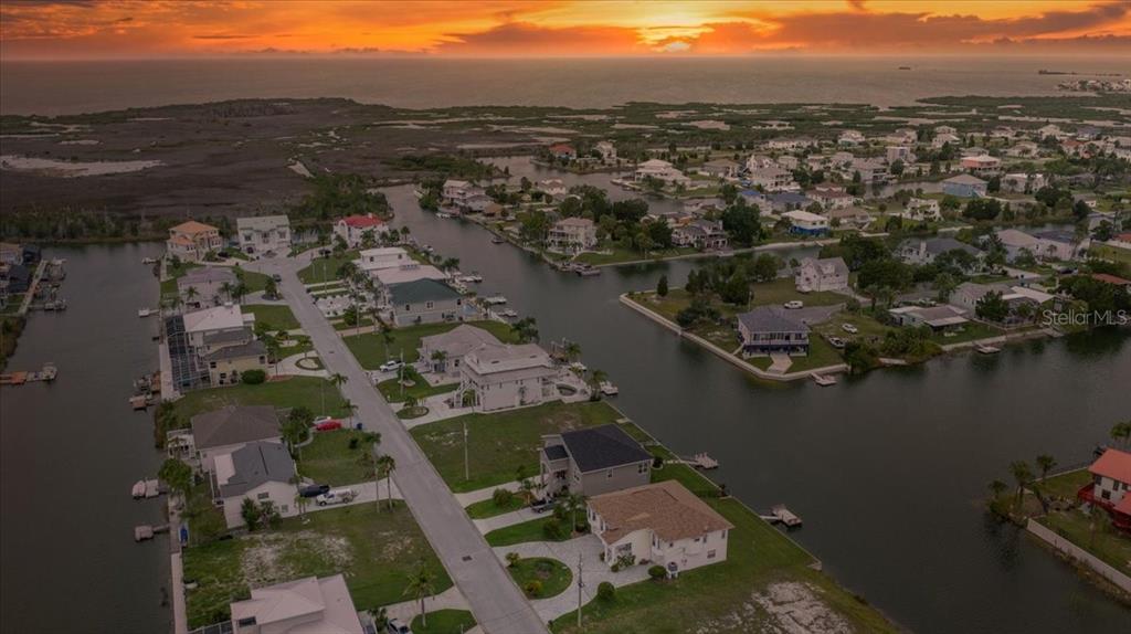 An aerial view of waterfront homes along canals leading to a sunset over the ocean — 3471 AMBERJACK DRIVE, HERNANDO BEACH, FL