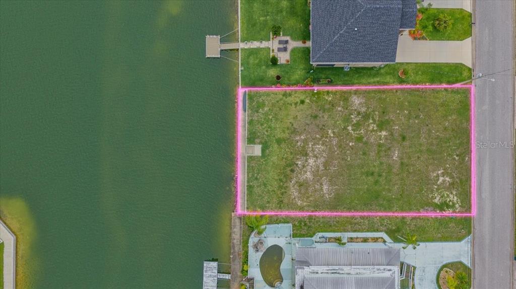 An aerial view shows a vacant waterfront lot outlined in pink next to existing homes — 3471 AMBERJACK DRIVE, HERNANDO BEACH, FL