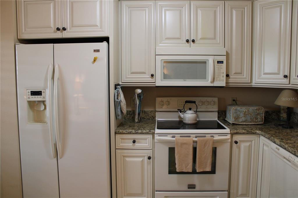 A kitchen features white cabinetry, granite countertops, and white appliances including a refrigerator and stove — 2725 TERRA CEIA BAY BOULEVARD UNIT 203, PALMETTO, FL