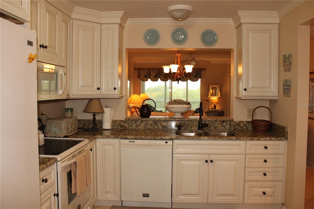 A kitchen with white cabinets, granite countertops, and a pass-through window overlooking a living area — 2725 TERRA CEIA BAY BOULEVARD UNIT 203, PALMETTO, FL