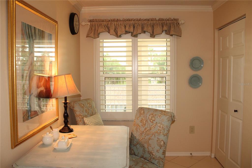 A small dining nook features a table, two patterned chairs, plantation shutters, and wall art — 2725 TERRA CEIA BAY BOULEVARD UNIT 203, PALMETTO, FL