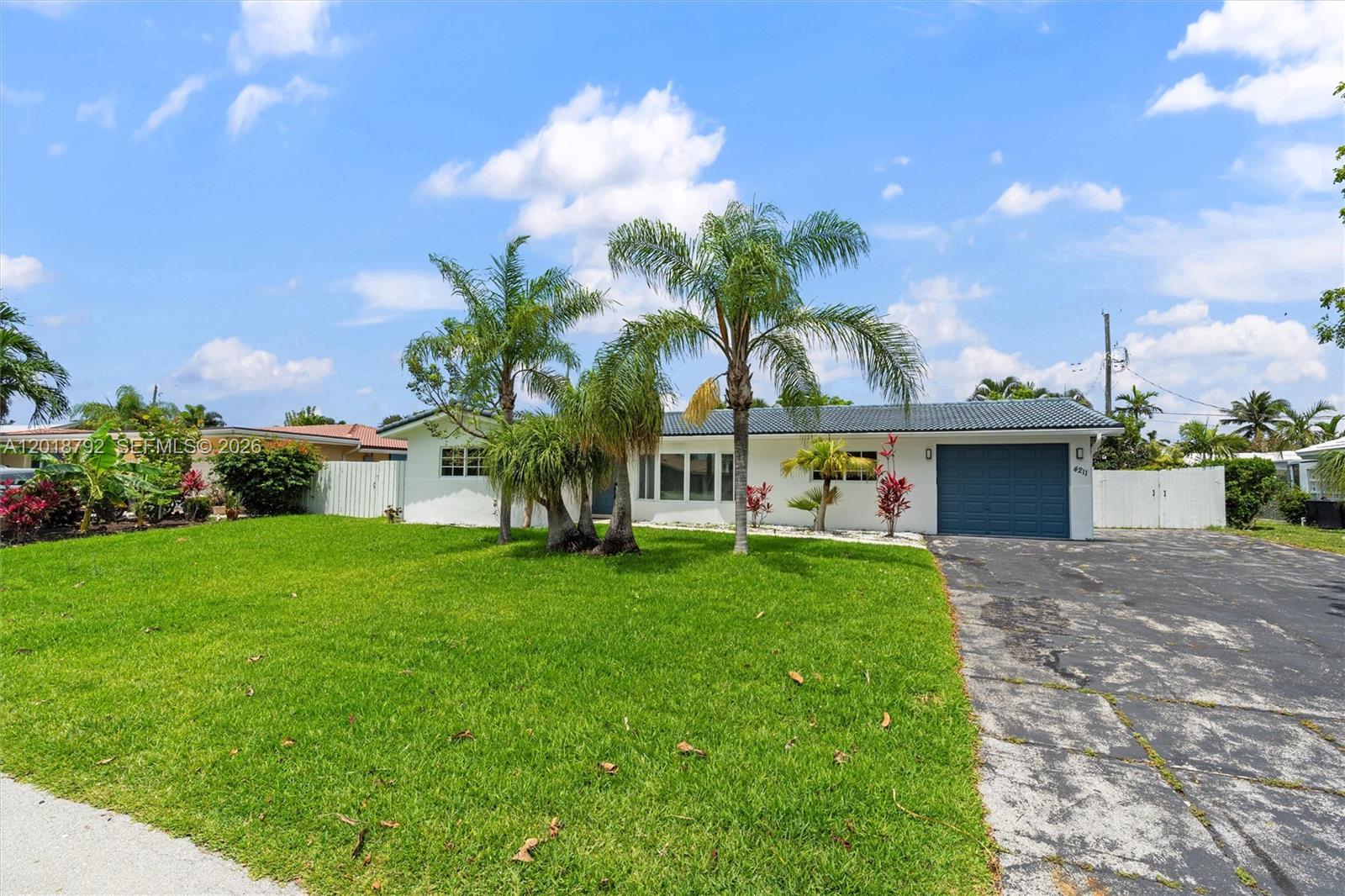 A single-story white house with a blue garage door and palm trees in the yard — 4211 NE 27th Ave, Lighthouse Point FL 33064, LIGHTHOUSE POINT, FL