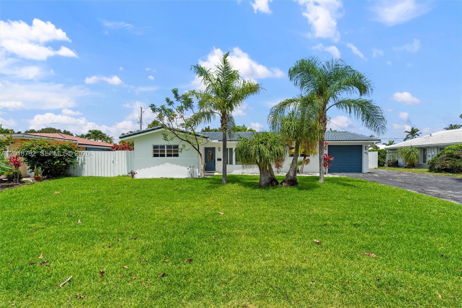 A single-story white house with a blue garage door and palm trees in the front yard — 4211 NE 27th Ave, Lighthouse Point FL 33064, LIGHTHOUSE POINT, FL