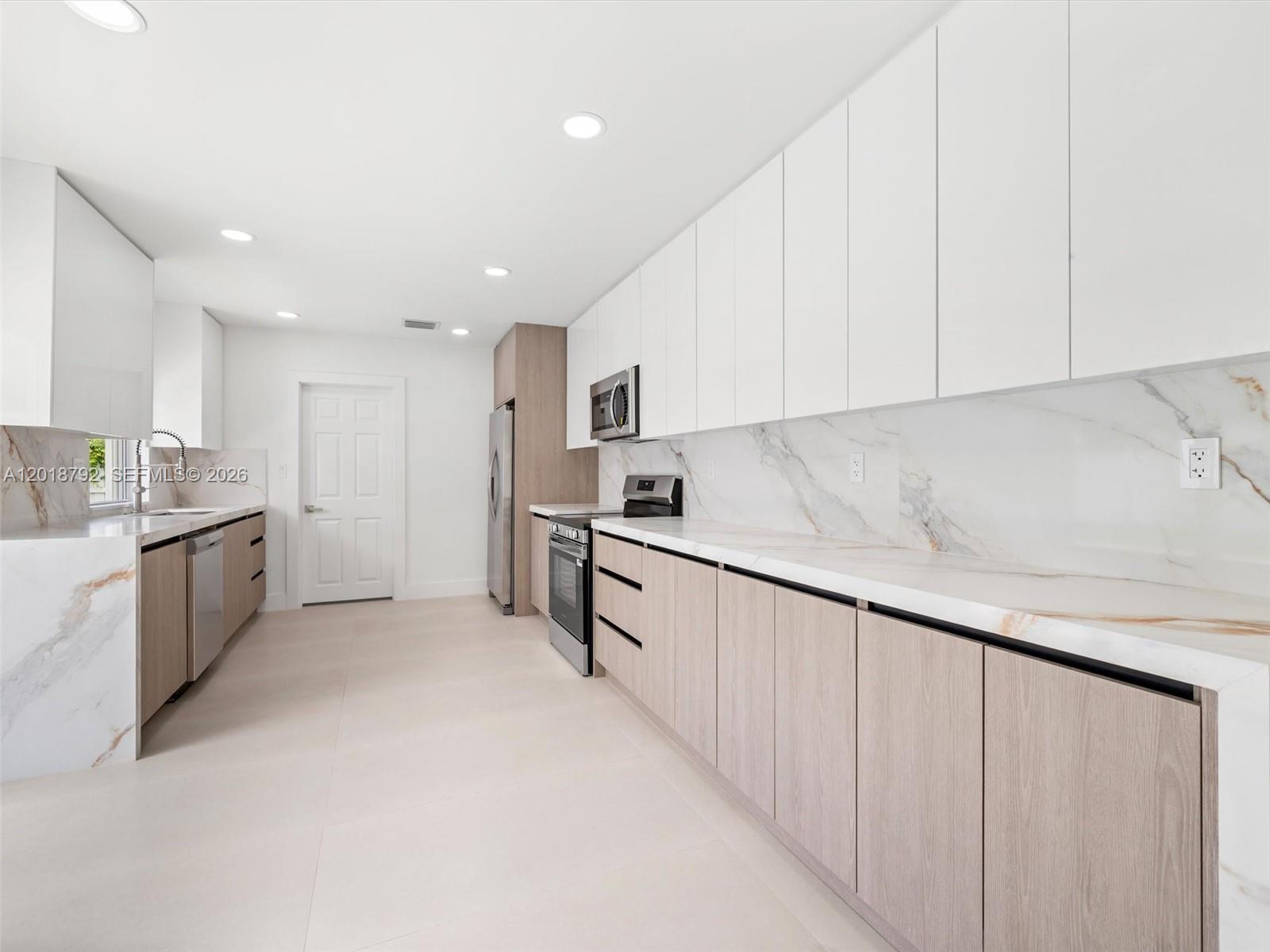 A modern kitchen features white upper cabinets, light wood lower cabinets, and marble-patterned countertops — 4211 NE 27th Ave, Lighthouse Point FL 33064, LIGHTHOUSE POINT, FL