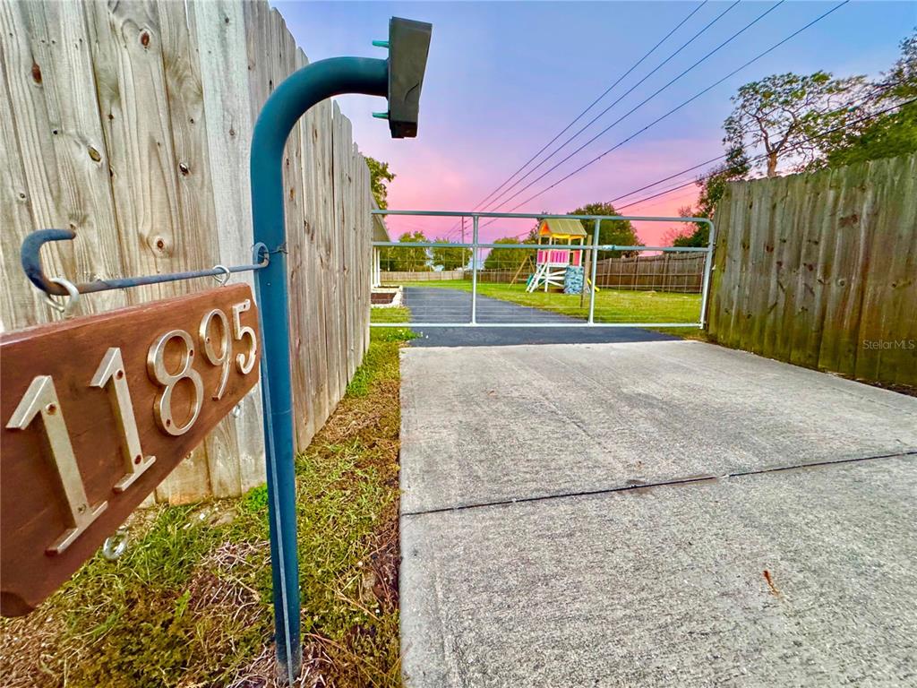A driveway leads to a metal gate and a wooden play set in a backyard — 11895 N BEARL TERRACE, DUNNELLON, FL