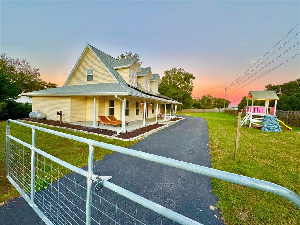 A yellow two-story house with a wrap-around porch sits beside a paved driveway and playground — 11895 N BEARL TERRACE, DUNNELLON, FL