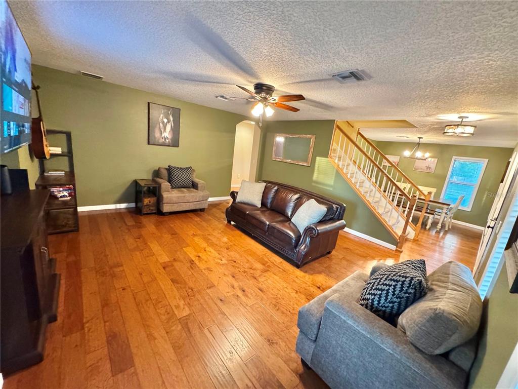 A living room with hardwood floors, olive green walls, a brown leather sofa, and stairs — 11895 N BEARL TERRACE, DUNNELLON, FL