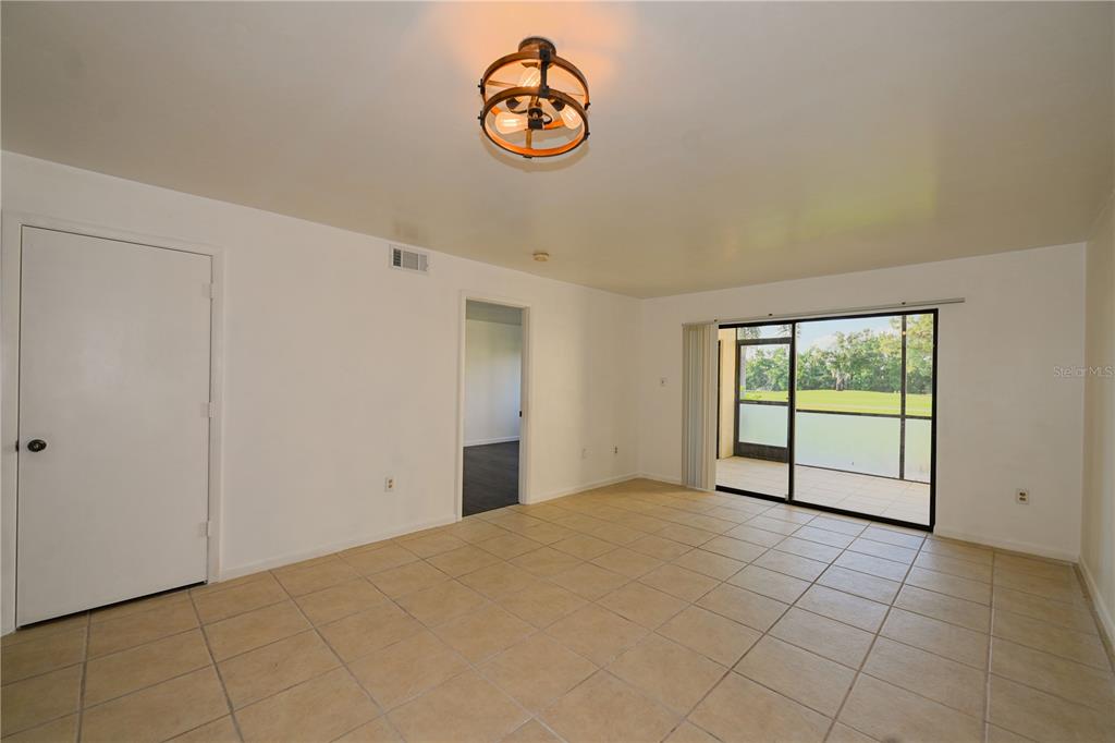 A living room with beige tile flooring, a central light fixture, and a sliding glass door — 4625 LONGWATER CHASE UNIT 113, SARASOTA, FL