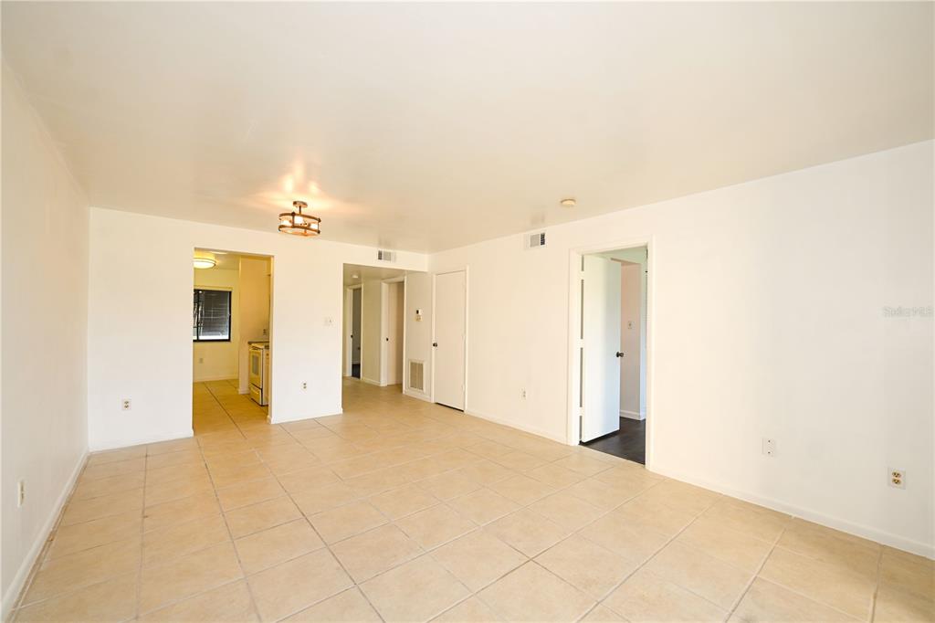 An empty room with beige tile flooring, white walls, and multiple doorways — 4625 LONGWATER CHASE UNIT 113, SARASOTA, FL