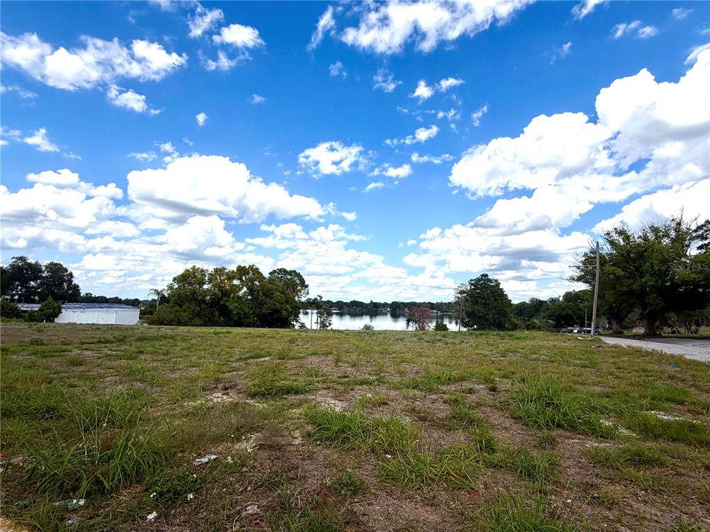 A grassy, undeveloped lot overlooks a lake under a bright, cloudy blue sky — 204 AVENUE D NE, WINTER HAVEN, FL