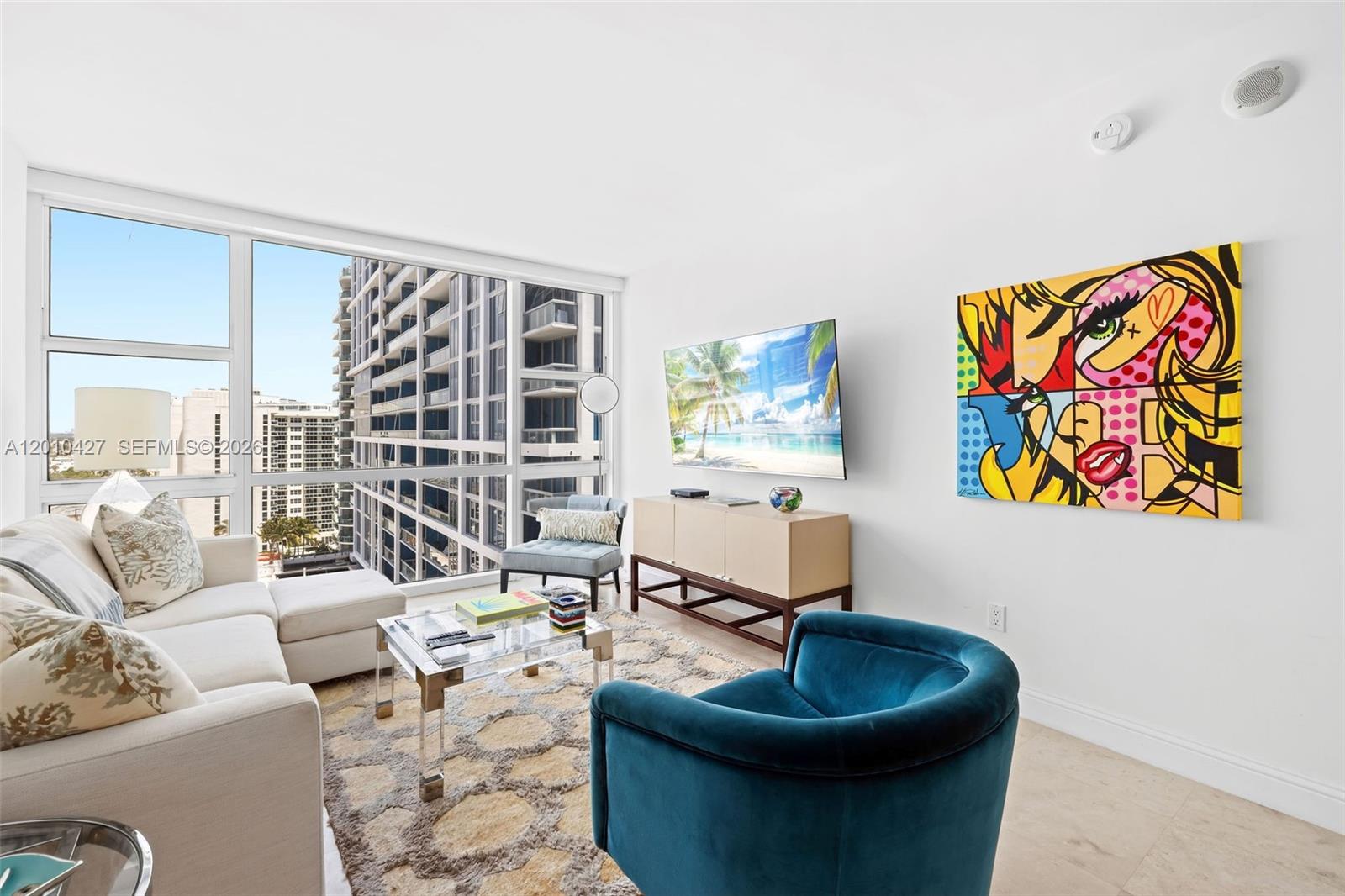 A living room features a white sofa, a blue armchair, and a large pop-art painting — 6801 Collins Ave # 1215, Miami Beach FL 33141, MIAMI BEACH, FL