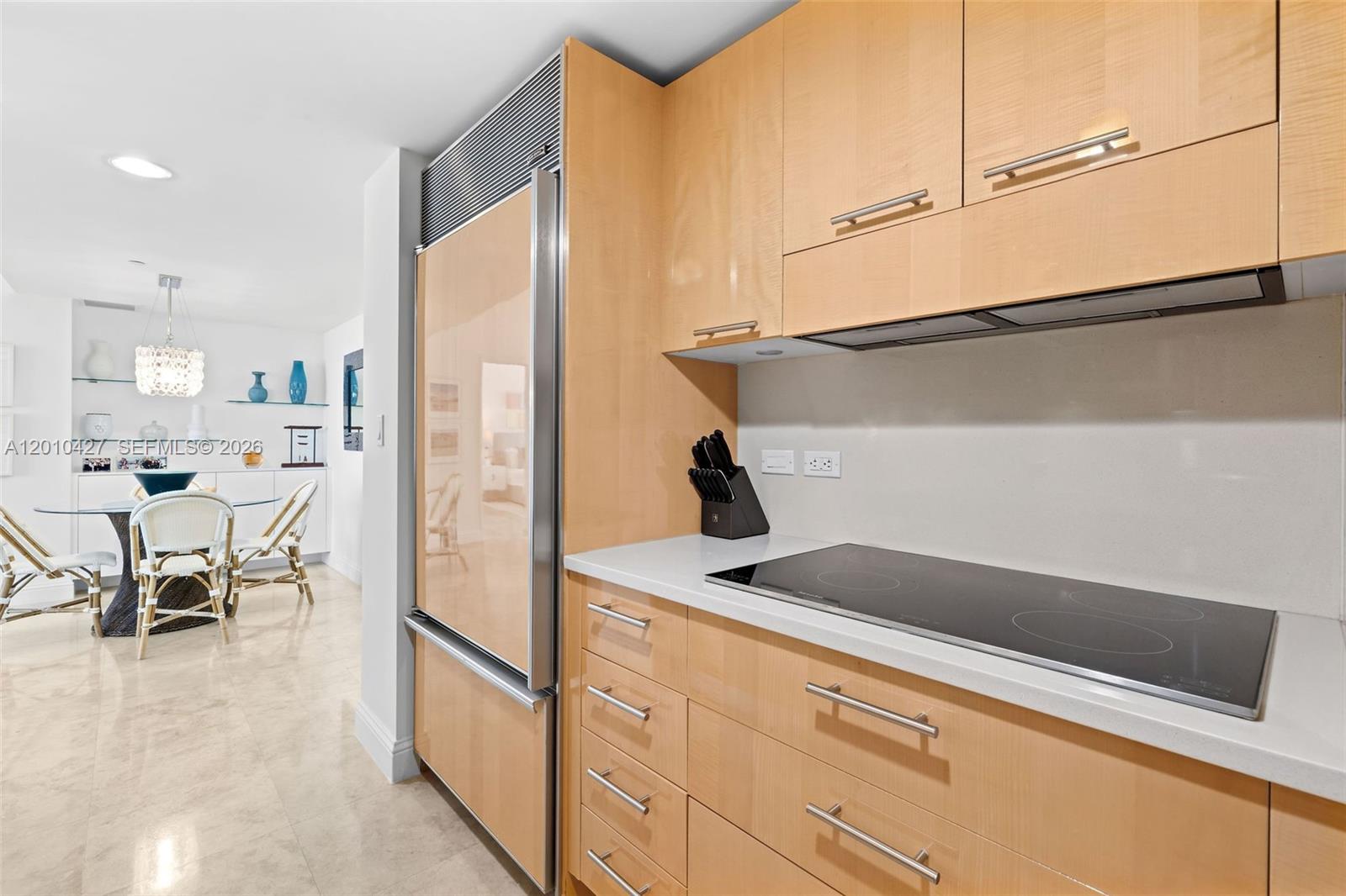 A kitchen features light wood cabinets, a stainless steel refrigerator, and a glass cooktop — 6801 Collins Ave # 1215, Miami Beach FL 33141, MIAMI BEACH, FL