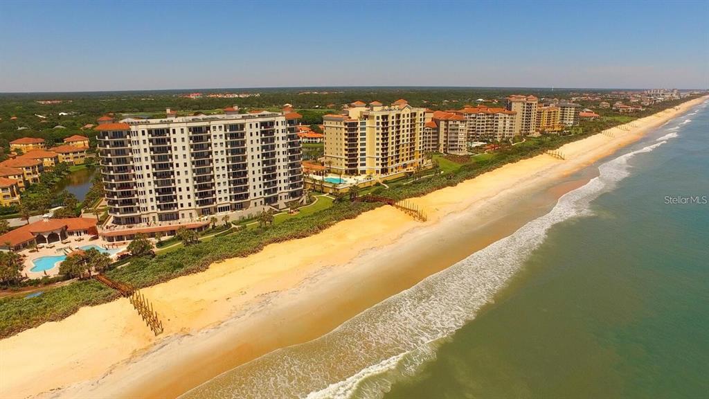 An aerial view shows large beachfront condominium buildings along a sandy coastline — 85 AVENUE DE LA MER UNIT 805, PALM COAST, FL