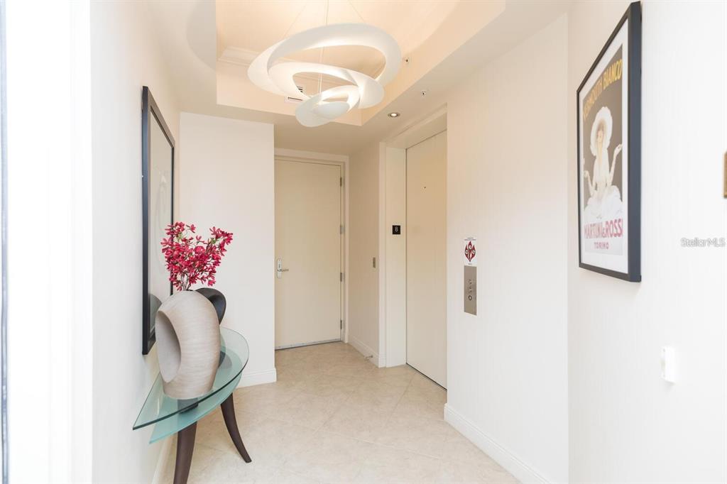 A bright entryway features a modern sculptural light fixture, a glass console table, and artwork — 85 AVENUE DE LA MER UNIT 805, PALM COAST, FL