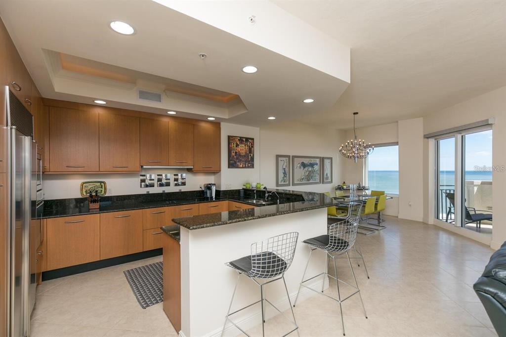 A modern kitchen with wood cabinets, granite countertops, and a breakfast bar overlooking the ocean — 85 AVENUE DE LA MER UNIT 805, PALM COAST, FL