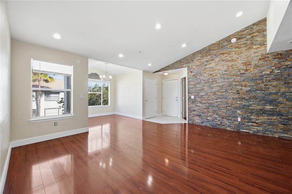 A living room with hardwood floors, recessed lighting, and a large stone accent wall — 2207 ANTIGUA PLACE UNIT 738, KISSIMMEE, FL