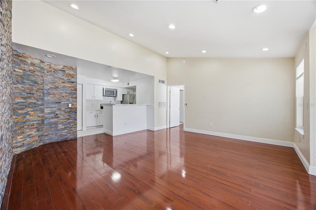 A living room with hardwood floors and a stone accent wall opens to a kitchen — 2207 ANTIGUA PLACE UNIT 738, KISSIMMEE, FL