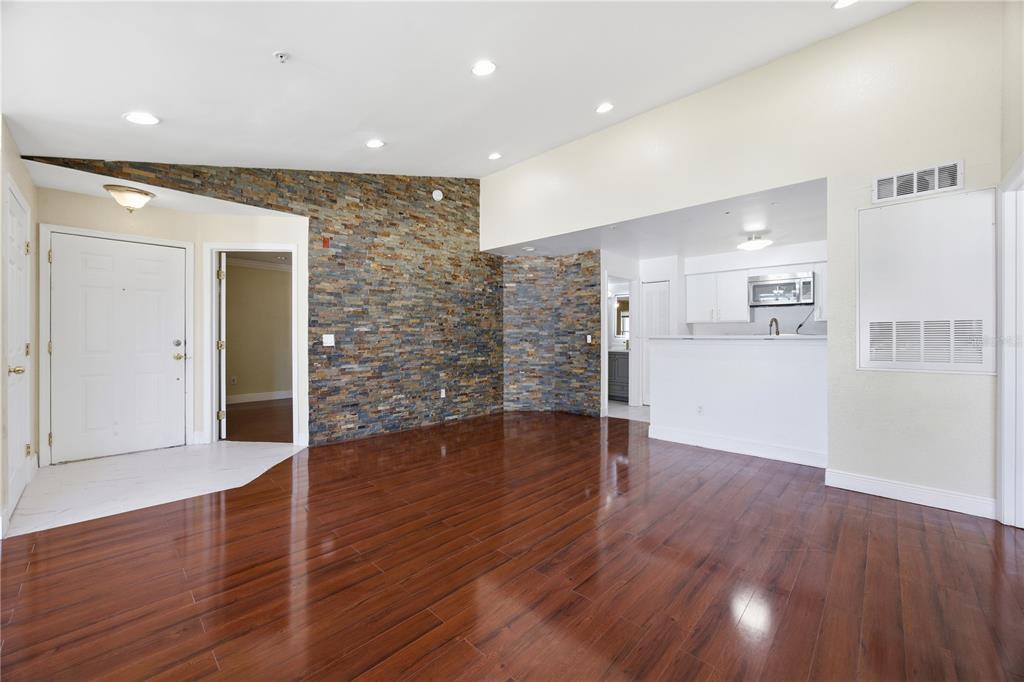 An open living area features dark wood flooring, a stone accent wall, and a kitchen — 2207 ANTIGUA PLACE UNIT 738, KISSIMMEE, FL