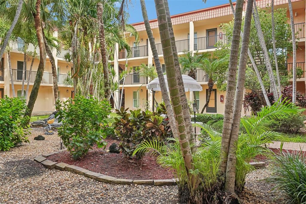 A multi-story apartment building exterior with a landscaped courtyard featuring palm trees and shrubs — 8911 BLIND PASS ROAD UNIT 319, ST PETE BEACH, FL