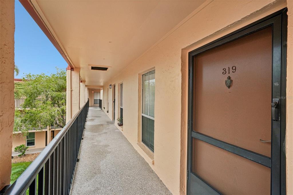 An exterior walkway with a metal railing leads to a brown door labeled 319 — 8911 BLIND PASS ROAD UNIT 319, ST PETE BEACH, FL