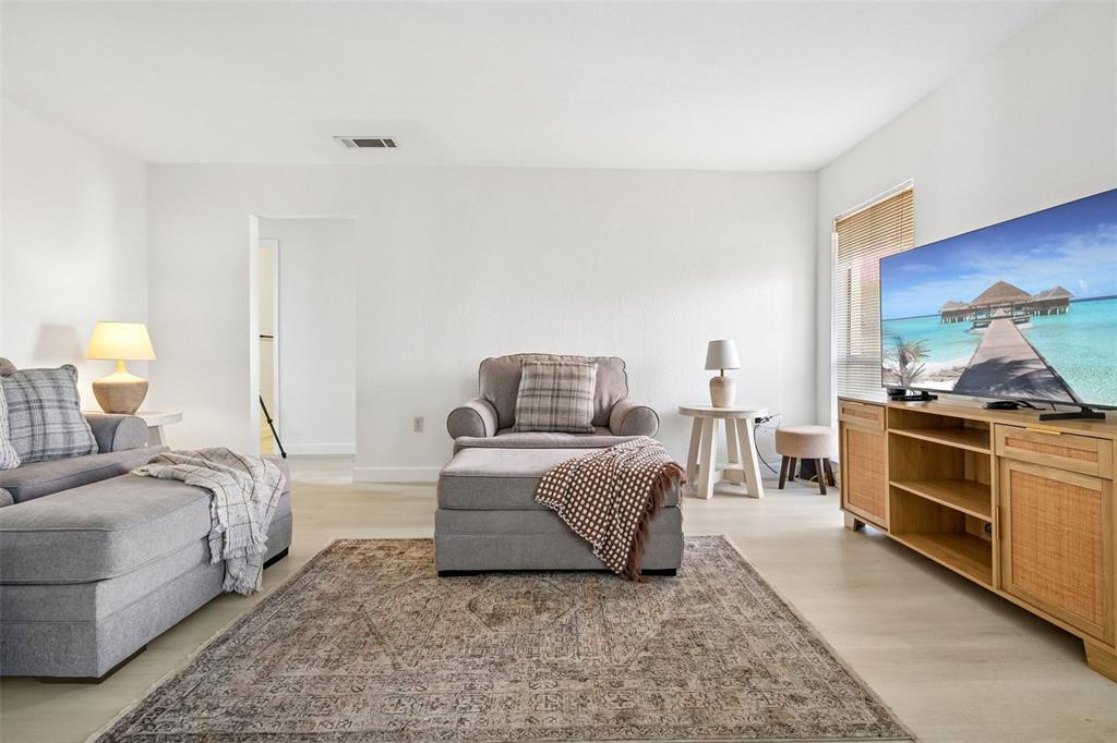 A living room features a gray sofa, an armchair with an ottoman, and a television console — 8911 BLIND PASS ROAD UNIT 319, ST PETE BEACH, FL