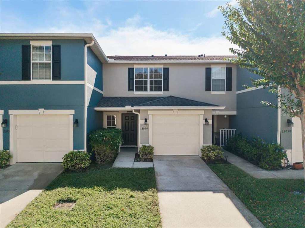 A two-story townhouse exterior features a beige facade, a garage, and a dark front door — 13054 LEXINGTON SUMMIT STREET, ORLANDO, FL