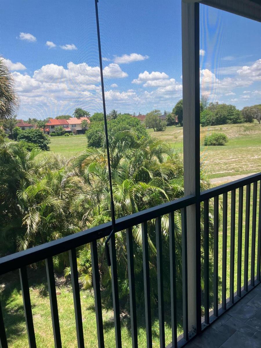 A view from a screened balcony overlooking a grassy field, palm trees, and distant houses — 3771 Environ Boulevard # 345, Lauderhill FL 33319, LAUDERHILL, FL