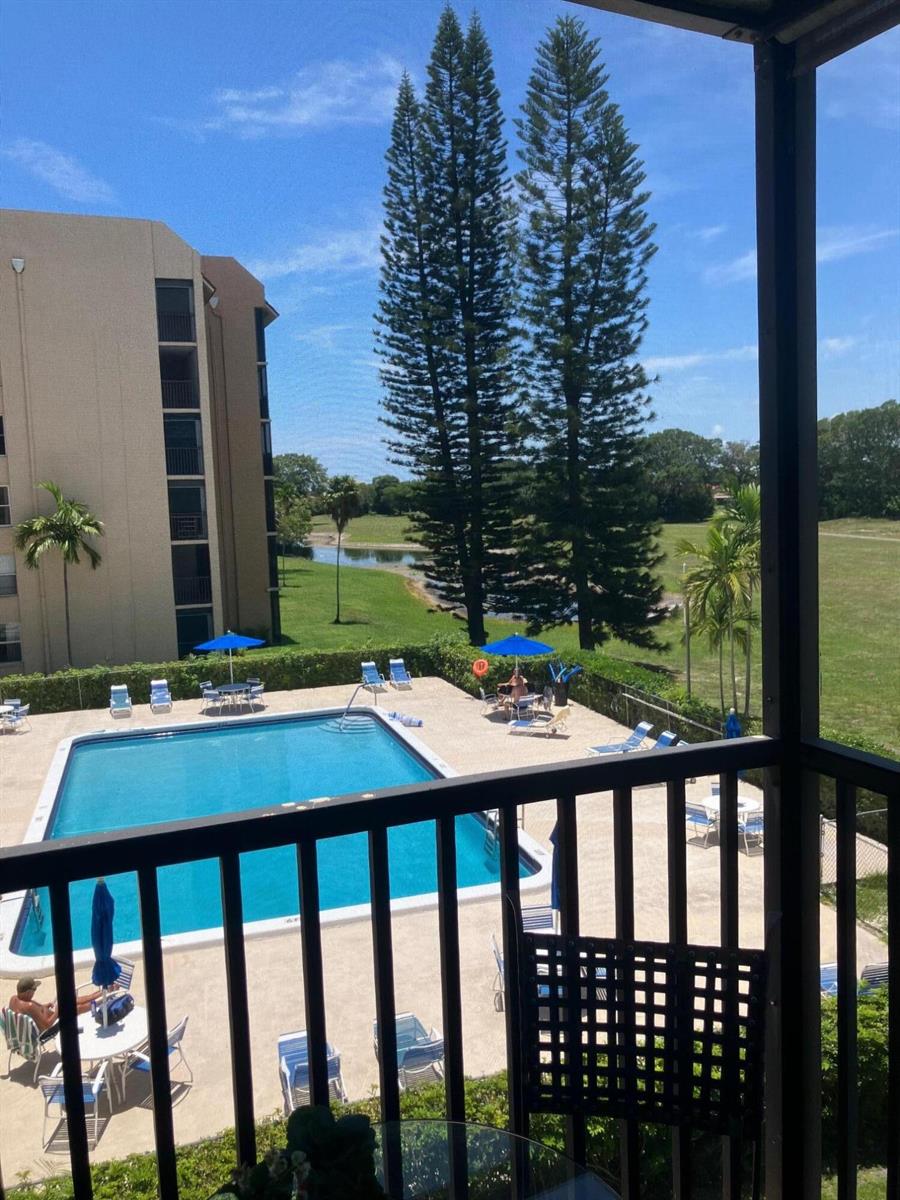 A balcony view overlooking a swimming pool, palm trees, tall pines, and a grassy field — 3771 Environ Boulevard # 345, Lauderhill FL 33319, LAUDERHILL, FL