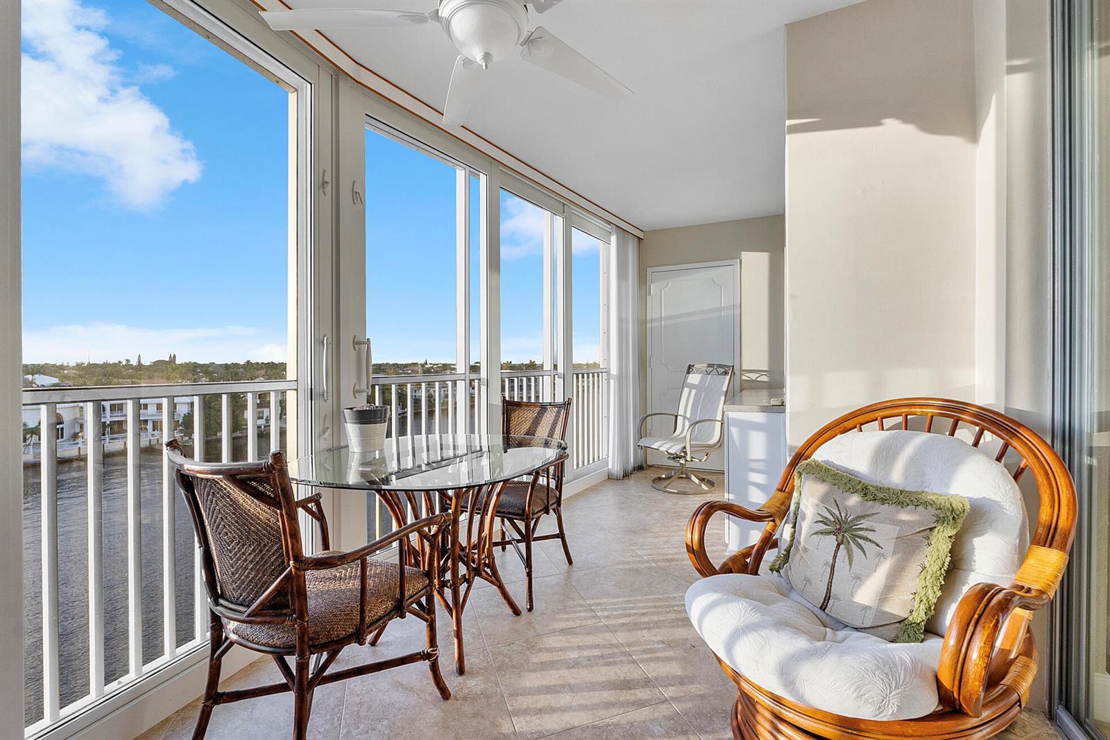 A sunroom with tile floors, wicker furniture, and large windows overlooking a waterway — 3310 S Ocean Boulevard # d, Highland Beach FL 33487, HIGHLAND BEACH, FL