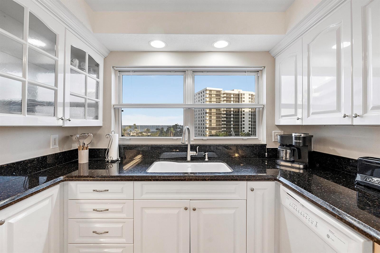 A kitchen features white cabinetry, dark granite countertops, a white sink, and a window view — 3310 S Ocean Boulevard # d, Highland Beach FL 33487, HIGHLAND BEACH, FL